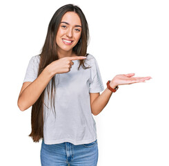 Canvas Print - Young hispanic girl wearing casual white t shirt amazed and smiling to the camera while presenting with hand and pointing with finger.