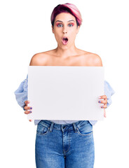 Poster - Young beautiful woman with pink hair holding cardboard banner with blank space scared and amazed with open mouth for surprise, disbelief face