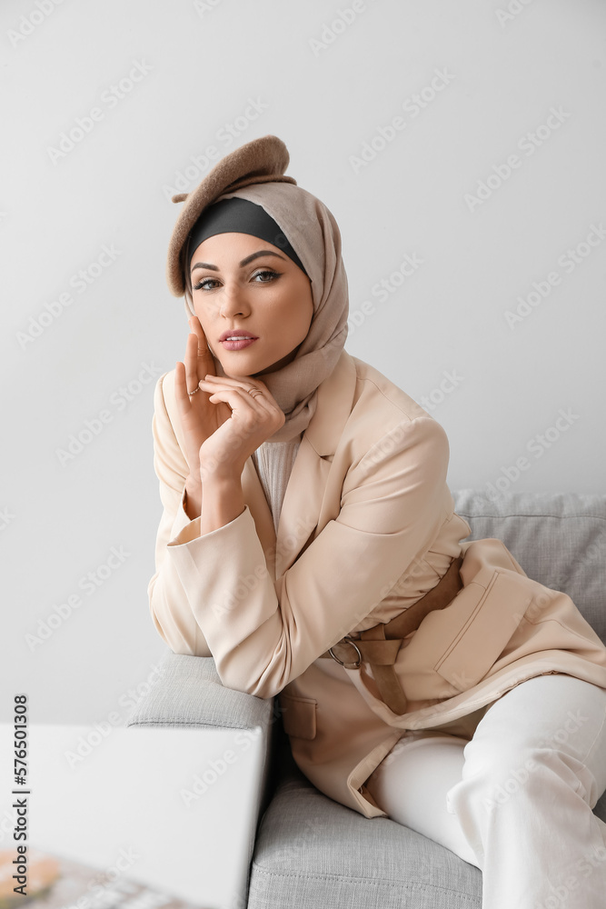Stylish Muslim woman sitting on sofa at home