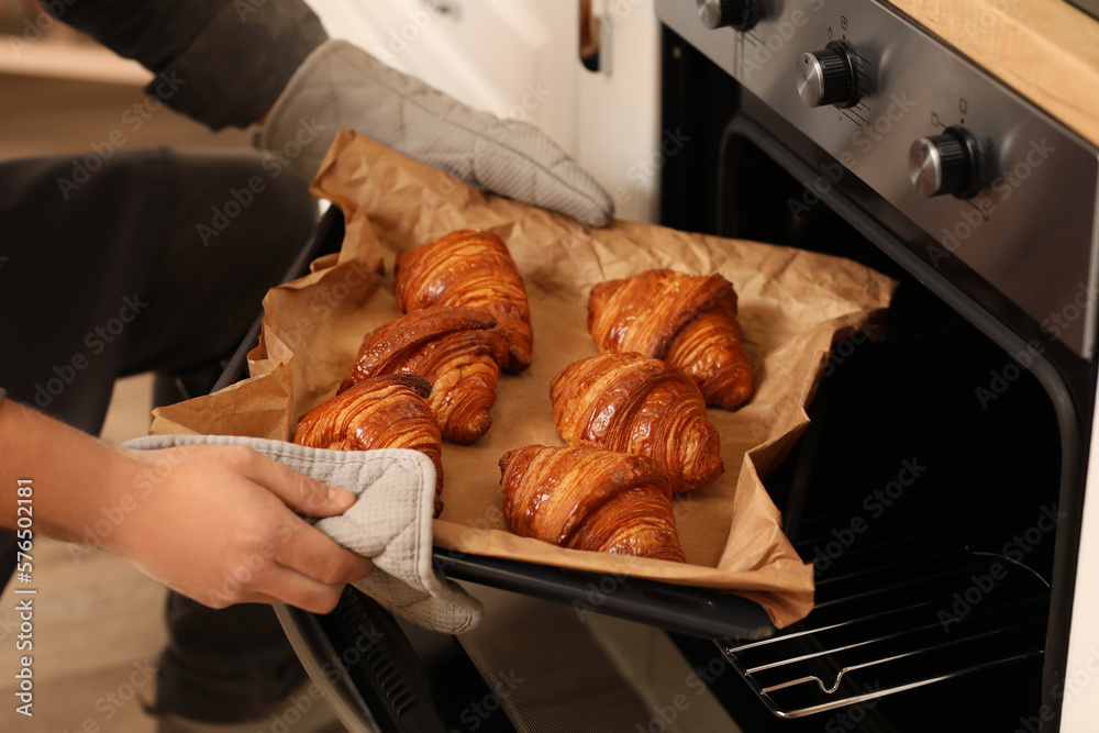 Male baker taking tray with croissants from oven in kitchen, closeup