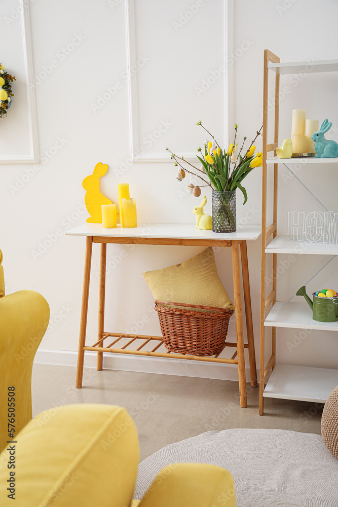 Vase with tulips, tree branches, Easter eggs, candles and rabbit on table in living room