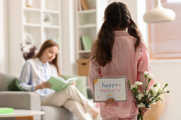 Wall Mural - Little girl with greeting card for Mother's Day and flowers at home, back view