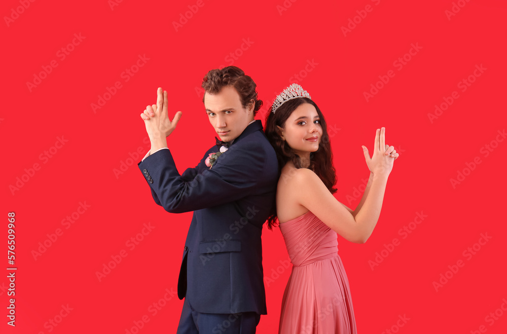 Beautiful couple dressed for prom showing gun gesture on red background