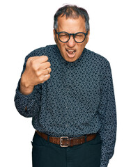 Wall Mural - Middle age indian man wearing casual clothes and glasses angry and mad raising fist frustrated and furious while shouting with anger. rage and aggressive concept.