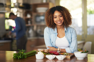 Poster - We like to keep our meals healthy. Portrait of a happy young woman preparing a healthy meal at home with her husband in the background.