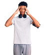 Young african american man wearing gym clothes and using headphones suffering from headache desperate and stressed because pain and migraine. hands on head.
