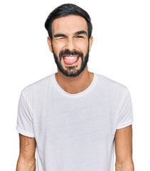 Wall Mural - Young hispanic man wearing casual white t shirt winking looking at the camera with sexy expression, cheerful and happy face.