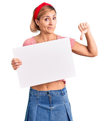 Poster - Young blonde woman holding blank empty banner with angry face, negative sign showing dislike with thumbs down, rejection concept