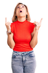 Sticker - Young blonde woman wearing casual clothes amazed and surprised looking up and pointing with fingers and raised arms.