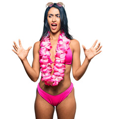 Wall Mural - Beautiful hispanic woman wearing bikini and hawaiian lei crazy and mad shouting and yelling with aggressive expression and arms raised. frustration concept.