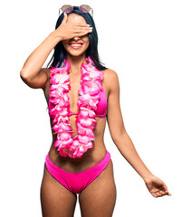 Wall Mural - Beautiful hispanic woman wearing bikini and hawaiian lei smiling and laughing with hand on face covering eyes for surprise. blind concept.