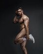 Naked handsome guy with american football ball. Naked American football player holding ball and his leg in studio. Bodybuilder playing sports.