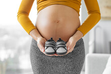 Pregnant Woman Expecting Baby Boy Holding Dark Blue Shoes In Gender Reveal During Pregnancy. Expectant Mother Showing Baby Bump Belly. Shopping Baby Clothing And Gender Reveal Concept