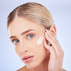 Skincare, face portrait and woman with cream in studio isolated on a blue background. Dermatology closeup, beauty cosmetics and young female model apply hydration lotion, creme or moisturizer product