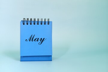 Wall Mural - Selective focus of May month desk calendar on blue background with spring leaves and copy space.