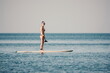 Sea woman sup. Silhouette of happy middle aged tanned woman in rainbow bikini, surfing on SUP board, confident paddling through water surface. Idyllic sunset. Active lifestyle at sea or river.