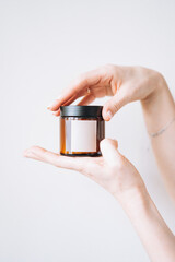 Women's hands hold glass jar with empty label on light background, mockup