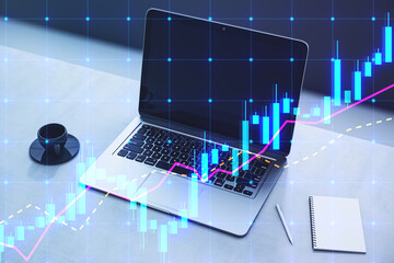 Poster - Close up of laptop on desktop with coffee cup, notepad and glowing candlestick forex chart hologram on blurry background. Trade and market concept. Double exposure.