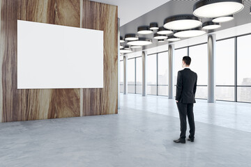 Aufkleber - Businessman back view looking at blank white poster with place for your logo or text on wooden wall in modern hall with stylish round lamps and city view background, mock up