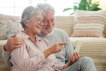 Wall Mural - Beautiful caucasian senior couple sitting on the floor at home using mobile phone, modern retired elderly people using technological devices to see funny videos