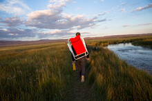 A Young Man Hikes With His Camping Chair Along The Owens River.