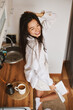© olga pink - Asian brunette woman in white in kitchen. Female holding, drinking morning cup hot coffee tea