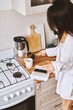 © olga pink - Asian woman in white clothes preparing morning beverage, pouring hot coffee from cezve to white cup