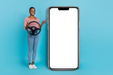 Full body photo of cheerful lady hand hold wheel indicate finger empty space ui phone display isolated on blue color background