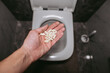 © Oleg - A hand throws pills into the toilet for flushing water