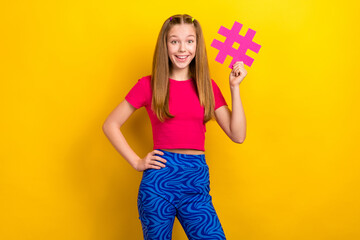 Wall Mural - Photo of young excited funny teenager girl wear pink t-shirt crop top touch waist blue retro trousers hashtag isolated on yellow color background