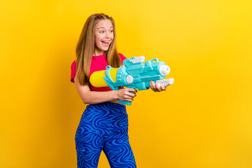 Wall Mural - Photo of careless teenager young lady wearing blue vintage sportive leggings shooting her new water splash gun isolated on yellow color background