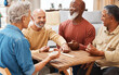 © Malik E/peopleimages.com - Senior men, friends and dominoes in board games on wooden table for activity, social bonding or gathering. Elderly group of domino players having fun playing and enjoying entertainment at home