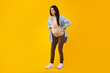 Full length shot of pregnant young woman suffering lover back pain, standing over yellow background, free space