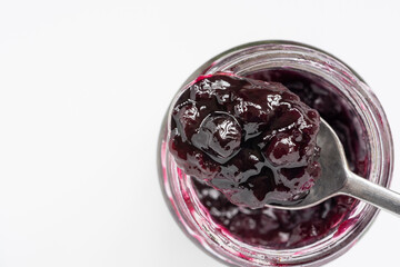 Delicious blueberry jam or fruit spread, on a spoon is resting on a glass jar on a white background. Top view.