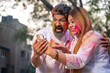 © PRASANNAPIX - young indian couple looking at smartphone and playing holi