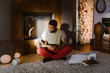 © Maskot - Young man reading book while sitting cross-legged at home