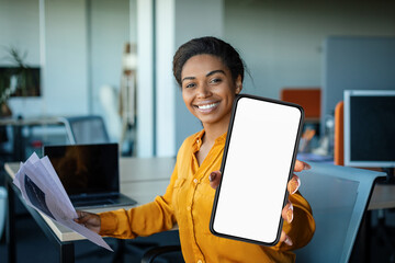 Wall Mural - Smiling black businesswoman demonstrating smartphone with blank screen while working in office