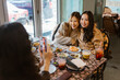 © Maskot - Woman photographing female friends sitting with food at restaurant
