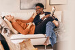 © Maskot - Happy multiracial couple having fun while reading books on sofa at home