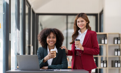 Wall Mural - Two Asian business women enjoy chatting during coffee breaks at their desks in a comfortable conference room