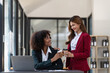 © Natee Meepian - Two Asian business women enjoy chatting during coffee breaks at their desks in a comfortable conference room