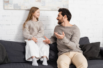 bearded man gesturing while talking to smiling daughter on couch in living room.