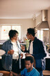 © Maskot - Mature man gesturing while talking to mother while standing at home