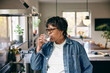© Maskot - Senior woman wearing denim jacket drinking water in kitchen at home