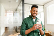 © Vadim Pastuh - Young Indian male employee, freelancer, businessman stands with a smartphone in hands, beaming with a smile as he looks at the screen, texting and messaging online