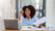 © amnaj - Happy businesswoman taking notes with laptop and document in office.