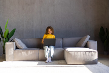 Pensive young woman using laptop computer while sitting on a couch at home