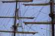 Masts, ropes, sails, ladder and hauled in sails of a historic sailing ship with a blue sky