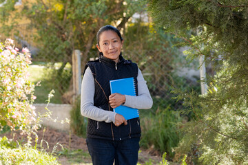 Portrait of latin woman with notebooks ready to study outside her home - Hispanic adult woman holding notebooks while smiling at the camera - Adult woman learning