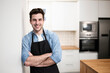 © carlesiturbe - handsome young man smiling in the kitchen wearing an apron - Portrait of a cheerful confident caucasian young man looking at camera with arms crossed